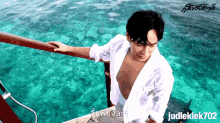a shirtless man leaning on a railing overlooking a body of water with judleklek702 written on the bottom