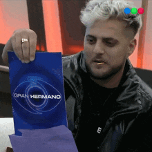 a man in a black jacket is holding up a sign that says gran hermano