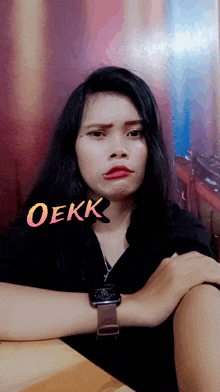 a woman sitting at a table with a watch on her wrist and the word oekk above her