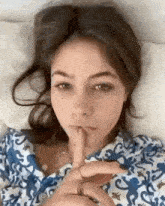 a woman is laying in bed with her finger to her lips .