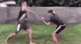 two men are standing next to each other in a grassy field and fighting .