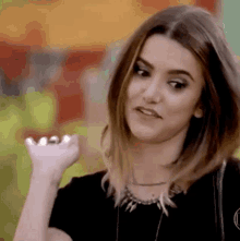 a woman is wearing a black shirt and a necklace and making a funny face