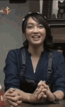 a woman sitting at a table with her hands folded in front of a sign that says tv