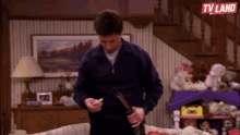 a man is holding a gun in a living room with a tv land logo above him