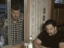 a man is smoking a cigarette while another man looks out a window .