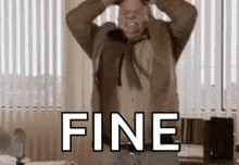 a man in a suit and tie is holding his head in a room with the word fine .