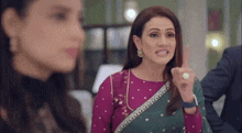 a woman in a purple top and green saree is making a funny face .
