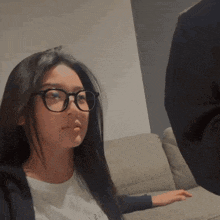 a woman wearing glasses is sitting on a couch with her hand on the arm of the couch