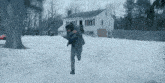 a man running in the snow in front of a house .