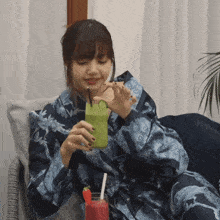 a woman in a blue robe is drinking a green smoothie with straws