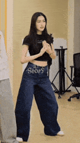 a woman in a black crop top and wide leg jeans has the word story written on her waist