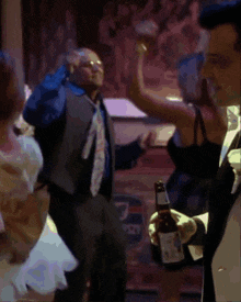 a man in a suit is dancing with a woman in a black dress who is holding a bottle of beer