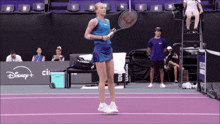 a woman holding a tennis racquet on a purple court with disney + in the background