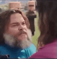 a man with a beard is talking to a woman in a pink shirt .