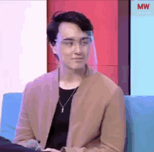 a young man wearing a face shield and glasses is sitting on a couch .
