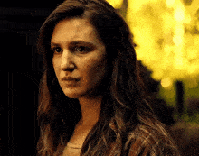 a woman with long hair and a plaid shirt is looking at the camera with a serious look on her face .