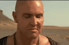 a close up of a bald man 's face with his eyes closed in the desert .