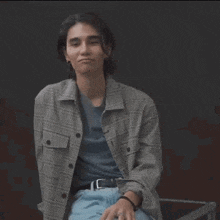 a young man in a plaid jacket and blue jeans is making a face .