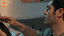 a man brushes another man 's hair with an ad for atv behind him