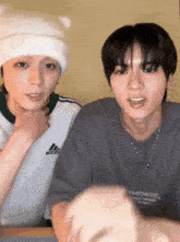 a man wearing an adidas shirt sits next to another man wearing a necklace