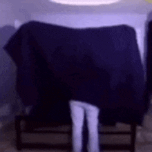 a person is standing in front of a couch with a blue blanket on it .