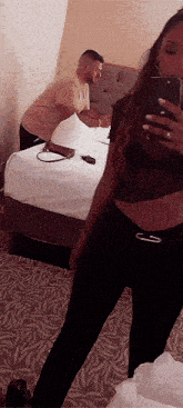 a woman is taking a picture of herself in a mirror with a man in the background