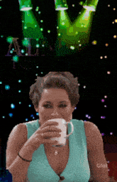 a woman drinking a cup of coffee in front of a sign that says ' alm ' on it