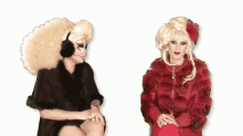 two drag queens are sitting next to each other talking to each other .