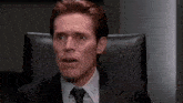 a man in a suit and tie is sitting in a chair making a funny face .