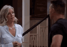 a man and a woman are standing next to each other in front of a staircase and talking to each other .