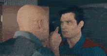 two bald men are standing next to each other and looking at each other in a room .