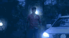 a man in a plaid shirt is walking towards a car in the dark .