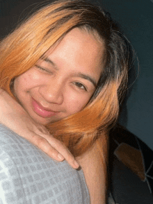 a woman with blonde hair is smiling with her eyes closed and her hand on her shoulder