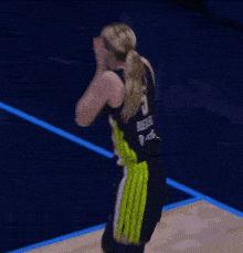 a female basketball player is covering her mouth with her hands while wearing a black and yellow uniform