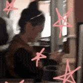 a woman is sitting at a table looking at her phone surrounded by pink stars ..