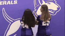 two cheerleaders are standing in front of a purple wall that says generals
