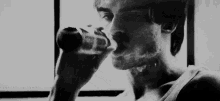 a black and white photo of a man drinking from a bottle .
