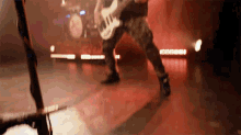 a man is playing a guitar on a stage with a drum set in the background