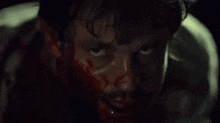 a close up of a man 's face with blood on it and a knife in his mouth .