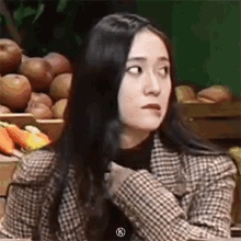 a woman with long black hair is wearing a plaid jacket and making a funny face .