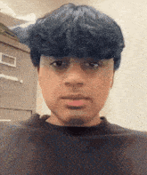 a young man with blue hair and a black shirt looks at the camera