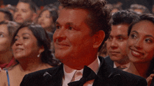 a man in a tuxedo is sitting in a crowd of people