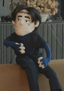 a puppet with a black shirt and blue gloves is sitting on a couch