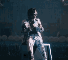 a man in a suit and sunglasses is sitting on a stool on a stage .