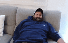 a man is laying on a couch wearing a blue adidas hoodie