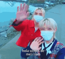 two people wearing face masks are standing next to each other and waving at the camera .