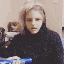 a woman in a black sweater is holding a blue container