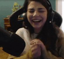 a woman wearing headphones is laughing in front of a microphone while sitting in a chair .