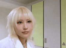 a woman with blonde hair and a white shirt is standing in front of a green wall .