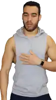 a man with a beard wearing a sleeveless hoodie holds his hand to his chest